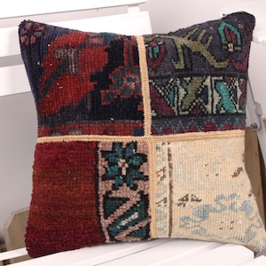 May include: Square decorative pillow with a patchwork design. The pillow features a mix of colors including red, navy, teal, and beige. The design includes geometric and floral patterns, creating a vintage or bohemian aesthetic.