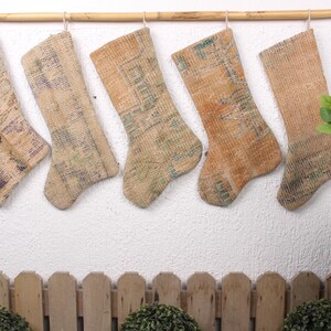 May include: Five beige and brown patterned stockings are hanging from a wooden rod against a white wall. The stockings are made of a woven fabric and have a rustic look.