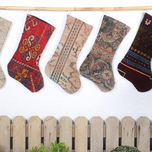 Può includere: Cinque calze di Natale colorate in tessuto fantasia sono appese a un'asta di legno. Le calze sono decorate con vari disegni, tra cui motivi geometrici, motivi floreali e forme astratte. Le calze sono un mix di rosso, beige, marrone e blu.