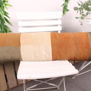 May include: A long, rectangular pillow with a patchwork design. The pillow features squares of various colors, including orange, beige, and olive green. The end of the pillow has vertical stripes. This decorative pillow is a home decor item.