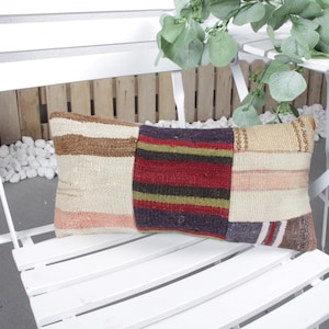 May include: A colorful patchwork pillow with stripes and geometric patterns in shades of brown, red, pink, and blue. The pillow is sitting on a white wooden chair.
