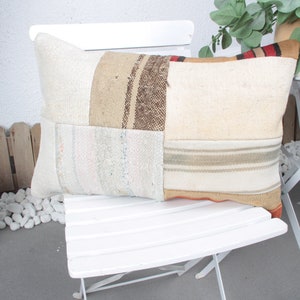 May include: A white, rectangular pillow with a patchwork design. The pillow is made of different fabrics in shades of beige, brown, and white. The pillow is sitting on a white chair.