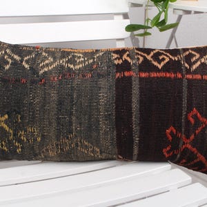 May include: A rectangular pillow with a black, brown, red, and beige woven pattern. The pillow has a geometric design and is made of a soft, textured fabric.