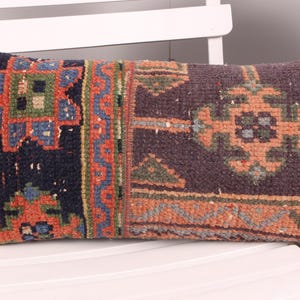 May include: Rectangular decorative pillow with a woven, patterned design. The pillow features a dark blue background with orange, green, and blue geometric shapes. The pillow is placed on a white chair.