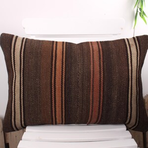 Peut inclure: Coussin rectangulaire marron avec des rayures verticales dans les tons marron, beige et orange. Le coussin est en tissu tissé et est posé sur une chaise blanche. Un article de décoration.