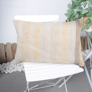 May include: A beige and white striped throw pillow with a textured woven fabric. The pillow is sitting on a white folding chair.