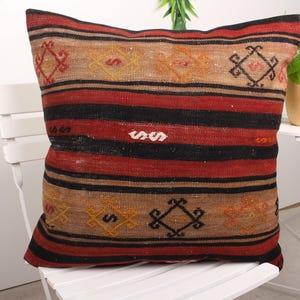 May include: A red, black, and beige striped throw pillow with a geometric pattern. The pillow is made of woven fabric and has a fringed edge.