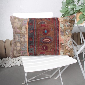 May include: A decorative pillow with a colorful, patterned design. The pillow is made of woven fabric and has a rectangular shape. It is sitting on a white chair.