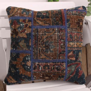 May include: Square cushion with a patchwork design. The cushion features a mix of colours including brown, blue, and red. The cushion is placed on a white chair.