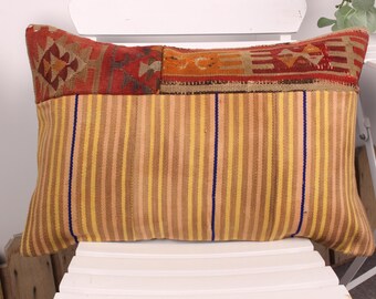 Può includere: Cuscino rettangolare con un motivo a righe nei toni del giallo, marrone e beige. La sezione superiore presenta un design geometrico in rosso, arancione e marrone. Una striscia verticale blu accentua il fronte.