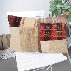 May include: A rectangular patchwork pillow with a beige background and colorful woven patterns in red, brown, and black. The pillow is sitting on a white chair.