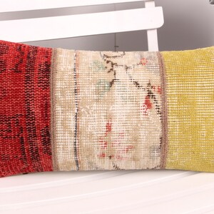 May include: Rectangular decorative pillow with a patchwork design. The pillow features sections of red, beige, and yellow fabric. The ends are red and navy blue. The pillow is placed on a white chair.