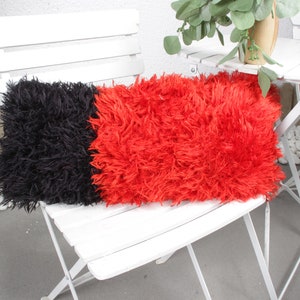 May include: A black and red fluffy pillow on a white folding chair. The pillow is made of two different colors of fur, one black and one red.