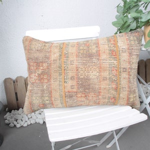 May include: A beige and orange patterned throw pillow with a woven texture sits on a white folding chair. The chair is on a patio with white gravel and a potted plant.
