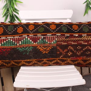 May include: A rectangular, patterned pillow with a dark brown base and intricate designs in orange, green, red, and white. The pillow features a patchwork design with geometric and floral motifs, suitable for home decor.