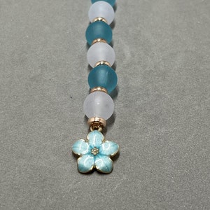 May include: A blue and white beaded keychain with a gold flower charm. The beads are round and have a frosted finish.