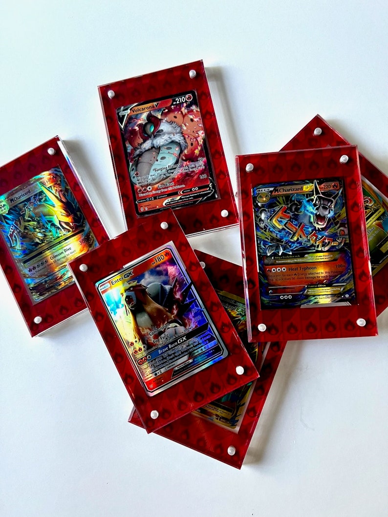 Może przedstawiać: Pięć kart kolekcjonerskich Pokemon w czerwonych akrylowych wyświetlaczach. Karty przedstawiają postacie Volcarona V, Entei GX, Charizard i Charizard. Karty są holograficzne i mają r&oacute;żne kolory, w tym czerwony, niebieski, ż&oacute;łty i zielony.