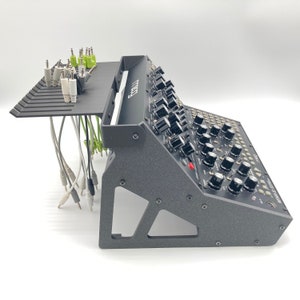 Puede incluir: Sintetizador negro con un soporte negro y un sistema de gestión de cables. El sintetizador tiene muchos botones y perillas. El soporte tiene un estante para guardar cables.