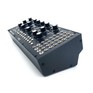 May include: A black synthesizer with numerous knobs, buttons, and input jacks. The word "moog" is printed on the front panel. The device has a rectangular shape with a slightly angled front.
