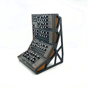 May include: A black modular synthesizer system with numerous knobs and switches, mounted in a wooden and black metal frame. The system is angled, with multiple modules stacked. The brand name "Moog" is visible on the modules.