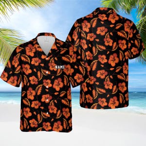 May include: Black Hawaiian shirt with orange hibiscus flowers and leaves. The shirt has a button-down front and a white collar. The word "NAME" is printed on the front. The shirt is short-sleeved and has a relaxed fit.