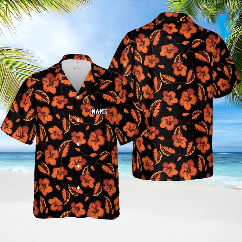 May include: Black Hawaiian shirt with orange hibiscus flowers and leaves. The shirt has a button-down front and a white collar. The word "NAME" is printed on the front. The shirt is short-sleeved and has a relaxed fit.