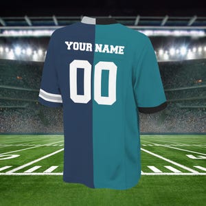 May include: A two-toned football jersey, split vertically with navy blue and teal. The back features the text "YOUR NAME" above the number "00" in white. The jersey has a white and gray stripe on the sleeve.