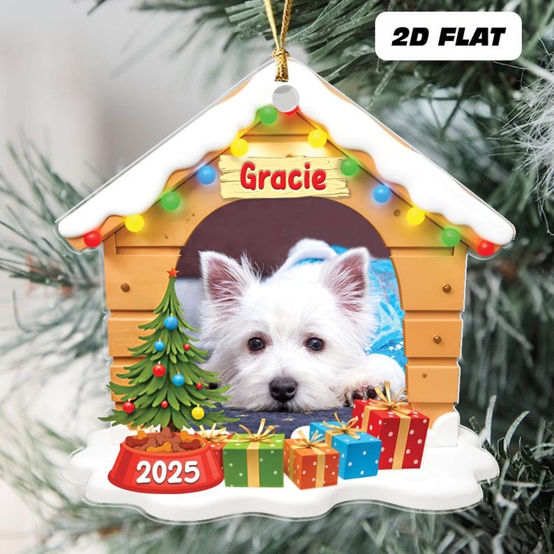 May include: A 2D flat Christmas ornament featuring a white dog named Gracie inside a dog house. The dog house is decorated with a string of colorful lights and a small Christmas tree. The ornament includes the year 2025 and several wrapped gifts.