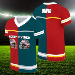 Op de afbeelding: Twee voetbaltruien, een rode en een teal, met een witte en grijze streep aan de onderkant. De rode trui heeft de naam "DAVID" op de rug. De teal trui heeft de tekst "HEART DIVIDED" en twee Amerikaanse voetbalhelmen met Amerikaanse vlaggen.