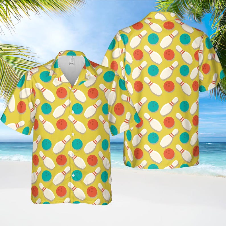 May include: Yellow bowling shirt with a repeating pattern of white bowling pins, red bowling balls, and teal bowling balls. The shirt has short sleeves and a button-down front. The background is a beach scene.