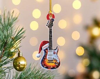 May include: A guitar-shaped Christmas ornament with a Santa hat that reads "Helen." The ornament has a colorful design with red, orange, and yellow hues. It hangs from a gold string, and is displayed on a Christmas tree.
