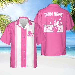 May include: Pink bowling shirt with white vertical stripes and a bowling pin graphic. The shirt has a button-up front and a collar. The back of the shirt features the text "TEAM NAME" above a bowling pin and ball graphic. The shirt is short-sleeved.