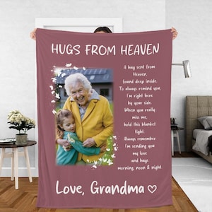 May include: A pink fleece blanket with a photo of a grandmother and granddaughter hugging. The blanket has the text "Hugs from Heaven" and a poem about sending love and hugs from heaven. The text "Love, Grandma" is at the bottom of the blanket.