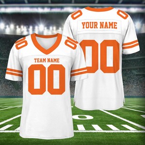 Puede incluir: Dos camisetas de f&uacute;tbol blancas con ribetes y n&uacute;meros naranjas. La camiseta de la izquierda tiene el texto "TEAM NAME" y el n&uacute;mero "00". La camiseta de la derecha tiene el texto "YOUR NAME" y el n&uacute;mero "00".