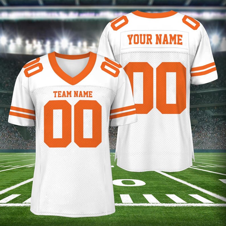 Puede incluir: Dos camisetas de f&uacute;tbol blancas con ribetes y n&uacute;meros naranjas. La camiseta de la izquierda tiene el texto "TEAM NAME" y el n&uacute;mero "00". La camiseta de la derecha tiene el texto "YOUR NAME" y el n&uacute;mero "00".