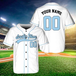 May include: White baseball jersey with blue trim and a blue number "00" on the front. The text "Sorority Name" is above the number in a blue and black script font. The back of the jersey has the text "YOUR NAME" above the number "00" in blue.