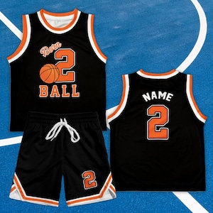 May include: Black basketball jersey and shorts set. The jersey features the words "Born Ball 2" with a basketball graphic. The shorts have a drawstring and the number 2. Orange and white accents trim the set.