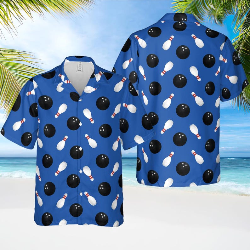 May include: Blue short-sleeved button-down shirt with a bowling theme. The shirt features a repeating pattern of black bowling balls and white bowling pins with red accents. The shirt is displayed on a beach background.