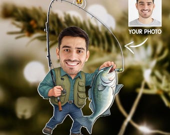 May include: A personalized fishing-themed ornament featuring a cartoon illustration of a man holding a large fish. The man is wearing a green vest and blue jeans, with a fishing rod in hand. A small photo is included. The ornament hangs from a gold string.