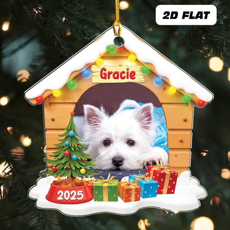May include: A personalized Christmas ornament shaped like a dog house, featuring a white dog named Gracie. The ornament includes a small Christmas tree, presents, and a bowl with "2025" on it. The ornament is decorated with colorful lights.