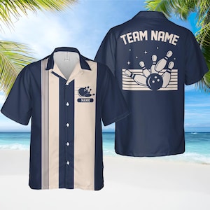 May include: Navy blue bowling shirt with a cream-coloured centre panel and vertical stripes. The shirt features a bowling ball and pins graphic with the text "NAME" on the front. The back of the shirt displays "TEAM NAME" above a bowling graphic.