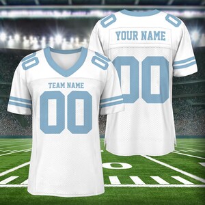 Puede incluir: Camiseta de f&uacute;tbol blanca con detalles azules. La camiseta tiene cuello en V y es personalizable con el nombre del equipo y el nombre del jugador. La camiseta se muestra en un campo verde con l&iacute;neas blancas.