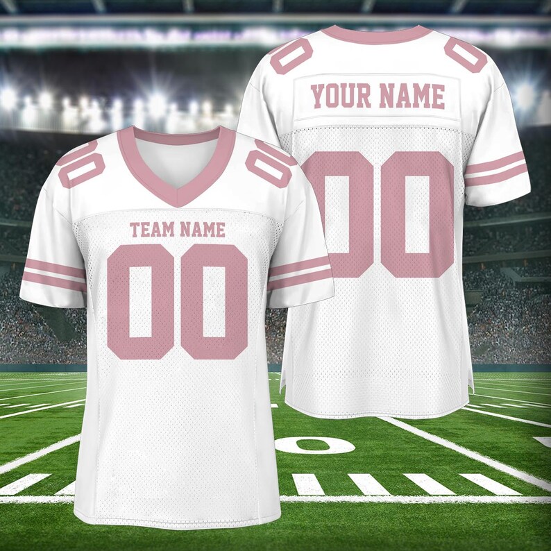 Puede incluir: Camiseta de f&uacute;tbol blanca con detalles en rosa. La camiseta tiene un n&uacute;mero rosa "00" en la parte delantera y el texto "TEAM NAME" encima del n&uacute;mero. La parte posterior de la camiseta tiene el texto "YOUR NAME" y el n&uacute;mero "00" en rosa.