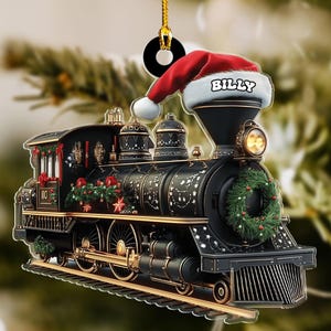 May include: A black and gold Christmas train ornament with a red Santa hat that says "Billy". The train has a green wreath and red floral accents. The ornament hangs from a gold string.