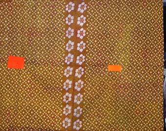 以下が含まれることがあります： マスタード色の織物で、白いひし形のパターンが繰り返されています。中央の垂直バンドには、赤いアクセントが付いた白い花の模様があります。端はオレンジ色の生地でトリミングされています。オレンジ色の正方形が2つ、織物に見えます。