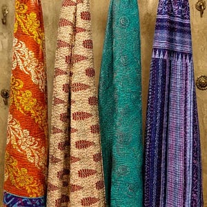 May include: Four rectangular scarves hanging side by side, featuring intricate kantha stitching. The scarves display vibrant patterns in orange, cream with red leaf motifs, solid teal with swirling designs, and a deep blue with geometric stripes.