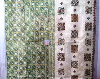 May include: A reversible quilt with a green and white floral pattern on one side and a cream-colored side with patterned squares. The quilt has a decorative border and is likely handmade.