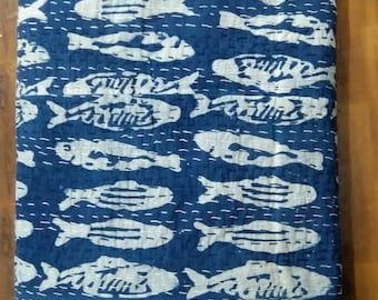 May include: A folded rectangular quilt featuring a deep blue background with a repeating white fish pattern. The fabric displays visible white running stitch quilting lines that create a grid-like texture across the entire surface of the textile.