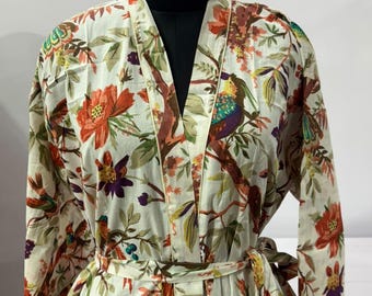 May include: A long-sleeved robe featuring a cream-coloured base with a vibrant botanical print of orange flowers, green leaves, and colourful birds. The garment includes a V-neckline, a matching fabric waist tie, and two front pockets on the lower section.