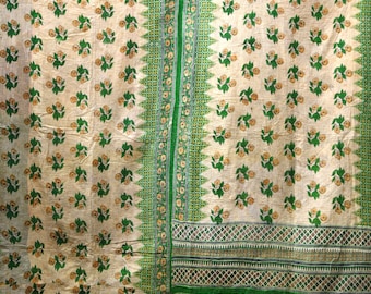 Op de afbeelding: Crèmekleurig textiel met een herhalend bloemmotief in groen en geel. De randen en een centrale verticale streep hebben groene geometrische ontwerpen. Het textiel heeft een vintage, handgemaakt uiterlijk.